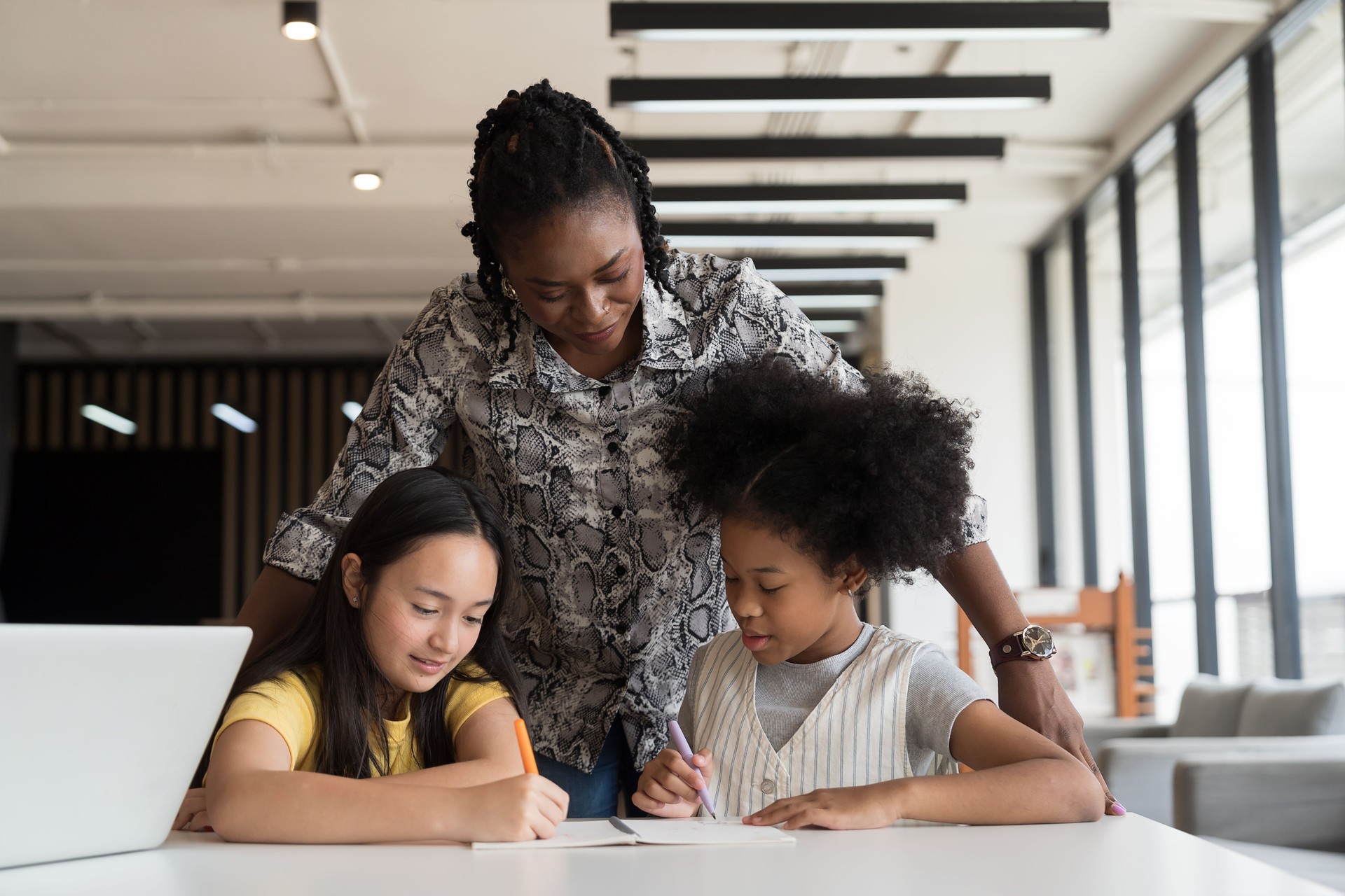 Female teacher teaching student in classroom, using laptop computer and take note or lecture on book